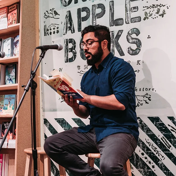 Jamil Jan Kochai sits on a stool in a bookstore and reads from his book.